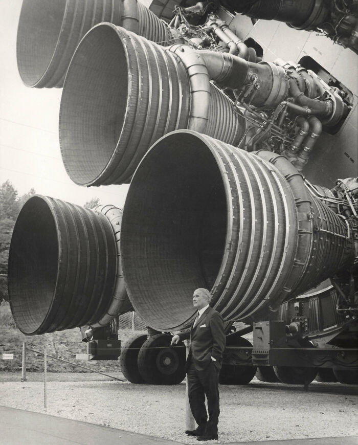 A man standing next to three enormous rocket engines, showcasing advanced and genius technologies from a past era.