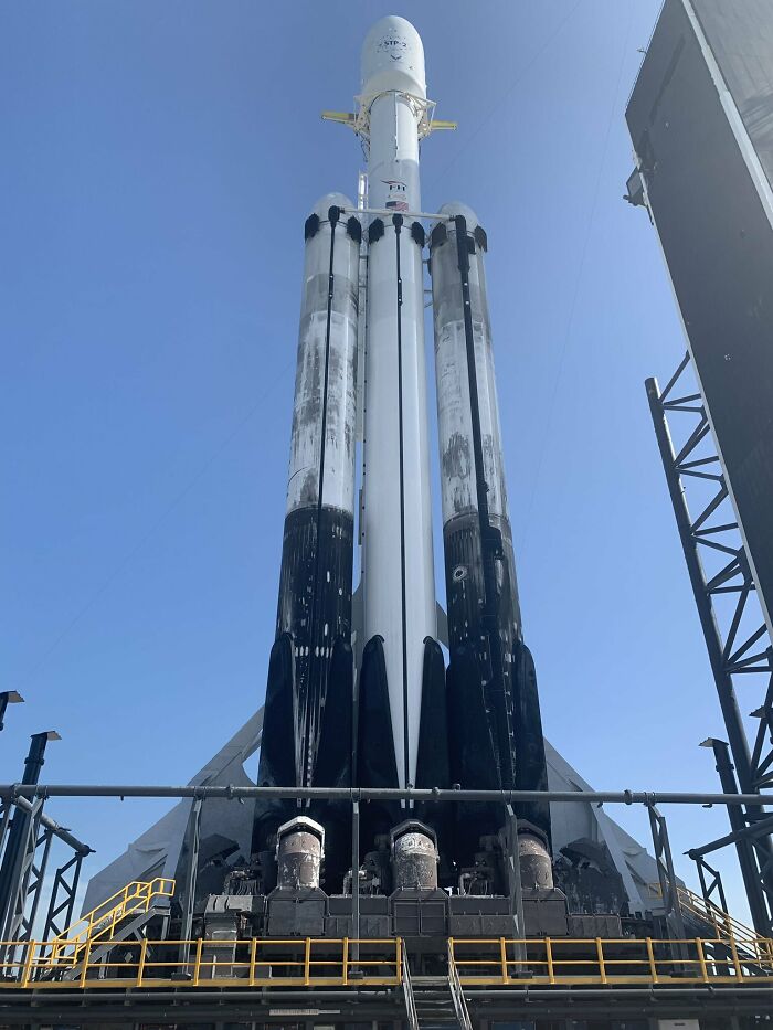 A Falcon Heavy rocket, an example of genius technologies, stands ready on the launchpad against a blue sky.
