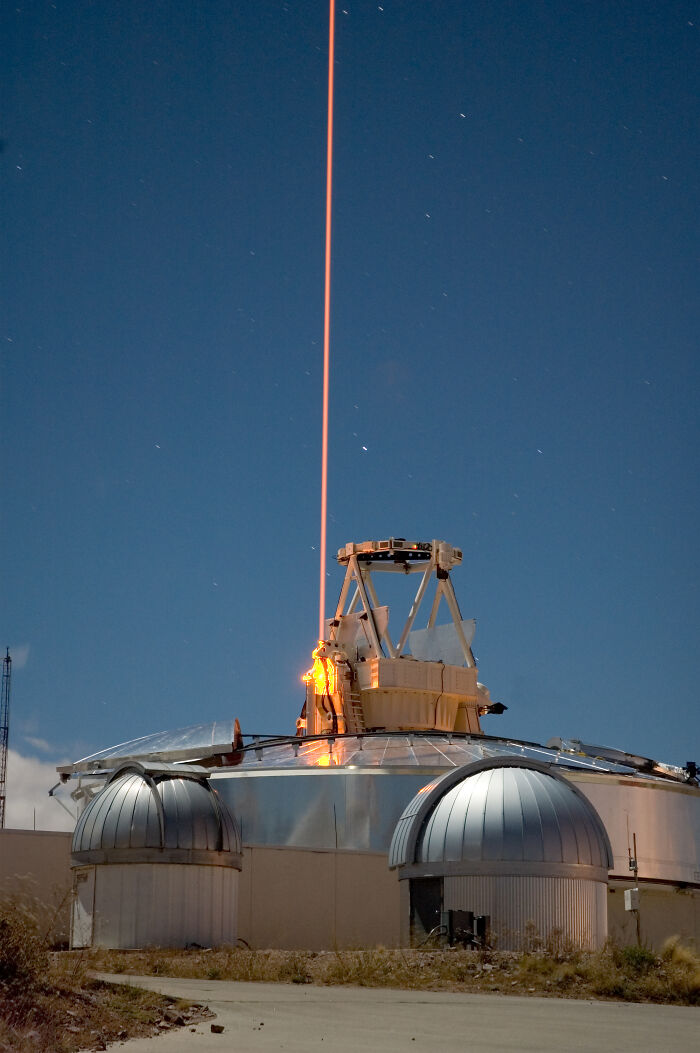 A powerful orange laser beam projects from an astronomical observatory into the night sky, demonstrating genius technologies.