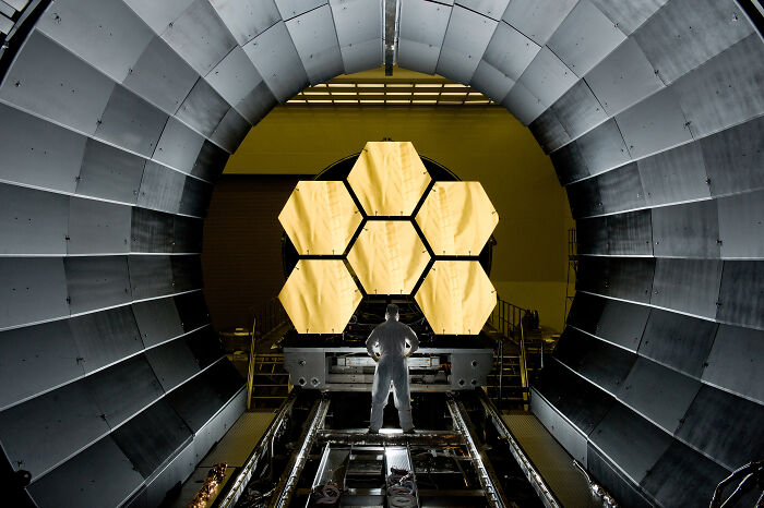 Man standing before the impressive gold mirrors of the James Webb Space Telescope, a genius technology.