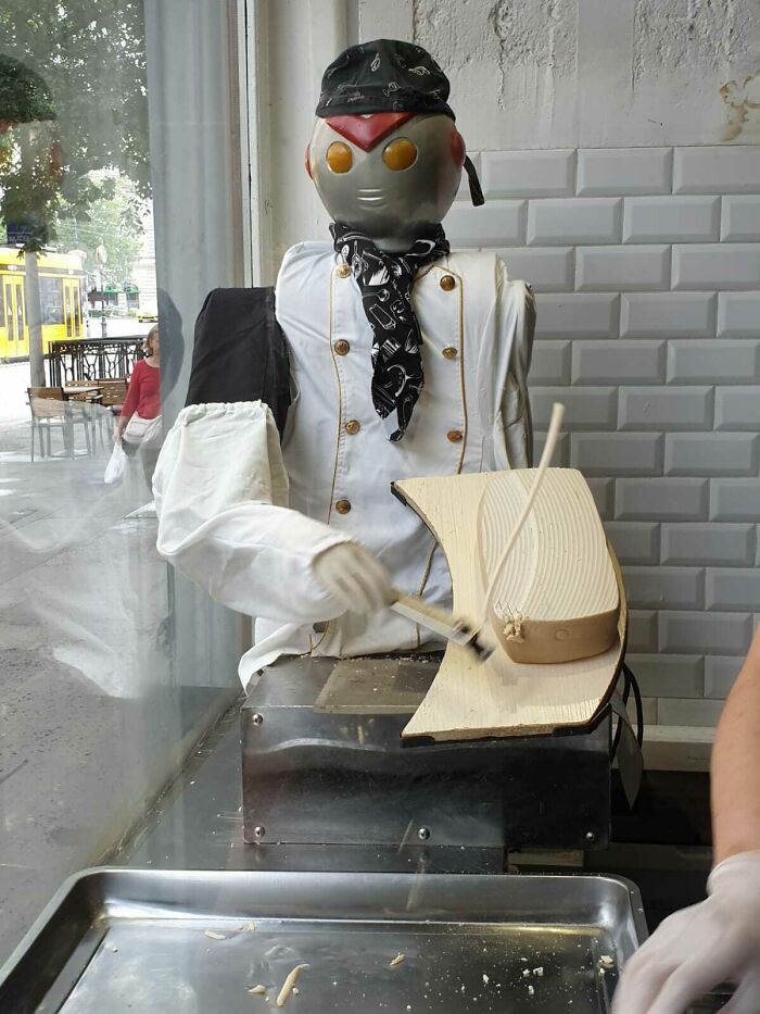 A chef robot preparing food in a shop window, an example of genius technologies.