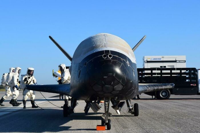 A sleek, black and white spaceplane on a runway with crew in hazmat suits, symbolizing advanced technologies in aerospace.