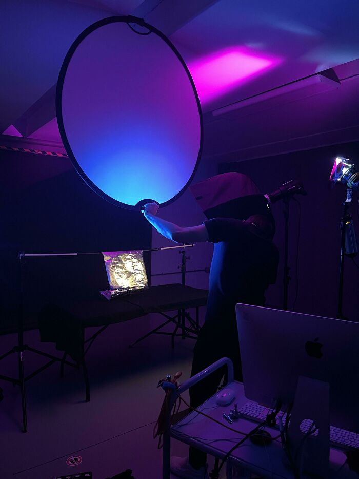 A person holding a large light reflector in a room illuminated with blue and purple lights, illustrating genius technologies for creative work.