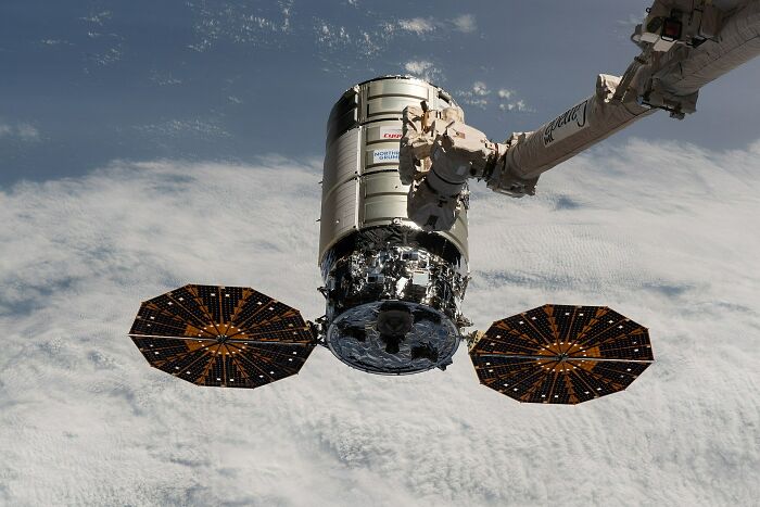 A Cygnus cargo spacecraft, an example of genius technologies, being grappled by the Canadarm2 in space.