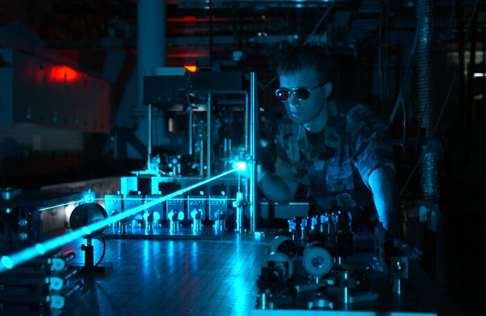 Satisfying and genius technologies: A scientist in sunglasses working with a blue laser setup.