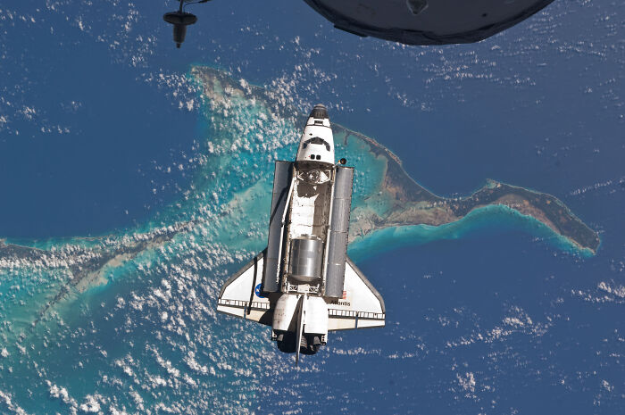 The Space Shuttle Atlantis soaring above Earth with turquoise islands below, a marvel of technologies that make everyday life easier.