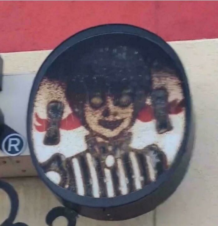 A faded and damaged circular sign showing a creepy and confusing cartoon character with dark hair and a striped shirt.