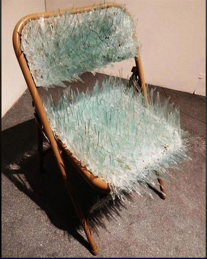 A folding chair covered in broken glass shards, a creepy and confusing furniture art piece.