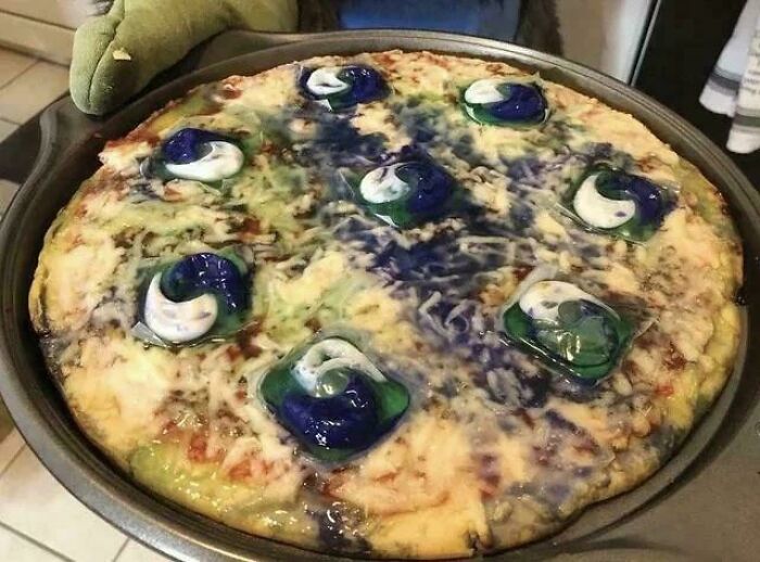 A creepy and confusing image of a pizza topped with colorful laundry detergent pods, needing a priest.