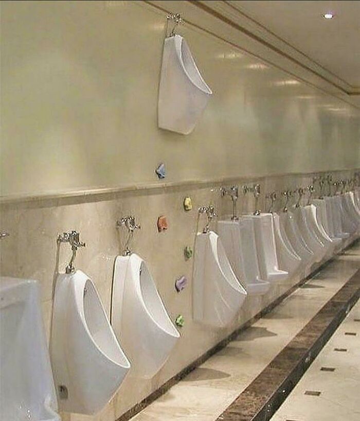 A confusing image of urinals installed at various heights on a bathroom wall, some very high, needing a priest.