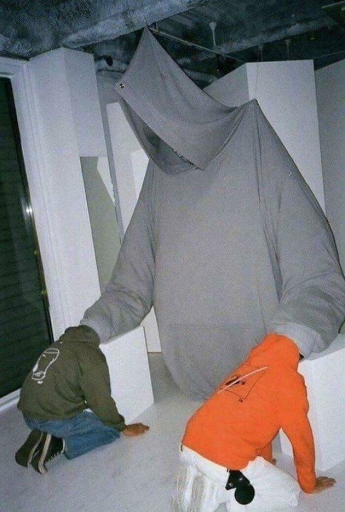 A creepy and confusing image of two individuals kneeling before a large, hooded figure made of fabric, needing a priest.