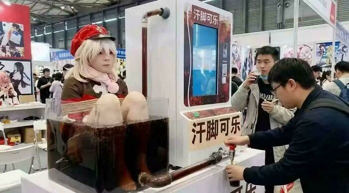 A confusing image of a person in a white elf-like costume submerged in a clear tank of dark liquid at an event, acting as a dispenser for drinks.