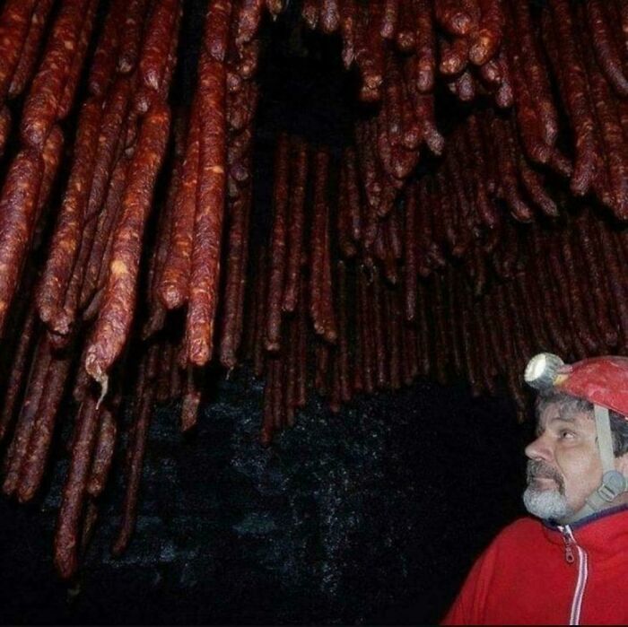 A man with a headlamp looking at hundreds of hanging sausages in a dark cave, a truly confusing image.