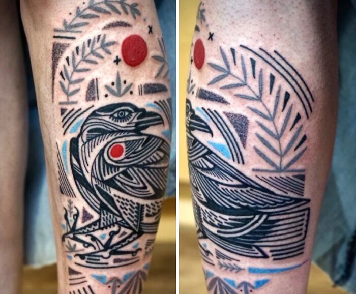 A leg tattoo art featuring a stylized black bird with red and blue accents, surrounded by geometric patterns, an inspiring example of tattoo art.