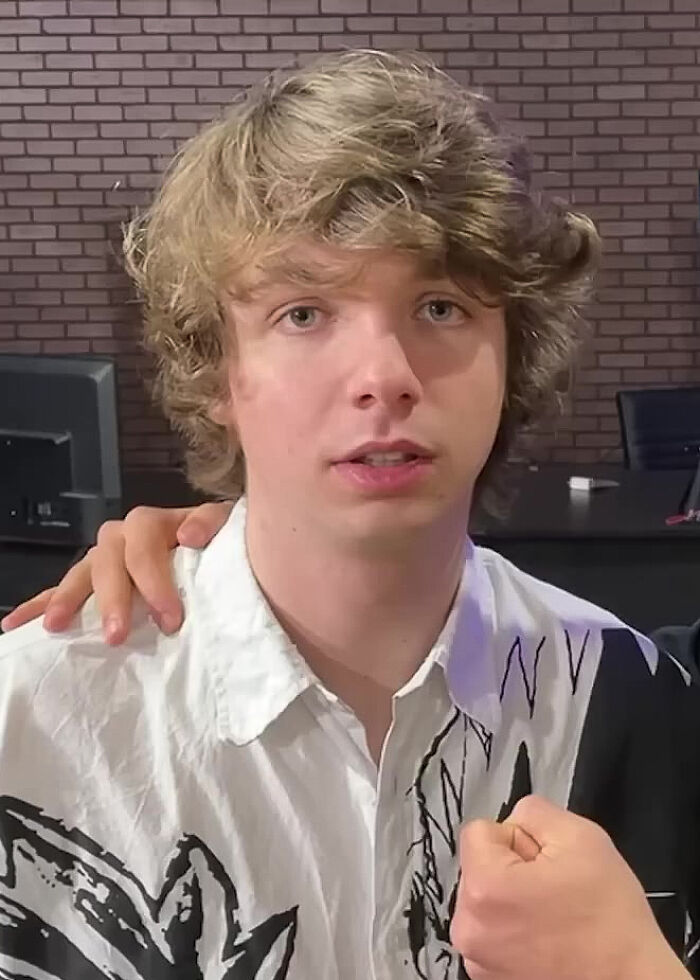 A close-up shot of Karl Jacobs looking at the camera, with a hand resting on his shoulder. Jacobs is wearing a black and white patterned shirt.