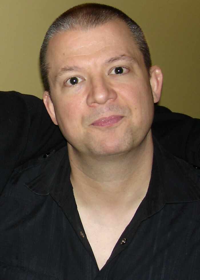 A headshot of Jim Norton with short hair, wearing a black shirt, looking directly at the camera. Jim Norton career highlights.