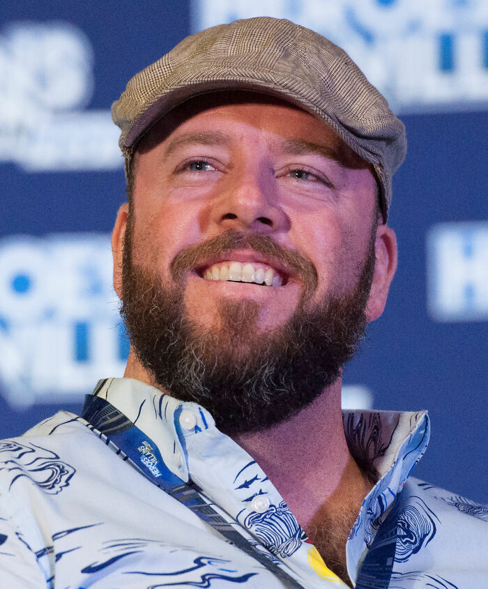 Chris Sullivan in a close-up, smiling with a beard and a flat cap, highlighting his career.