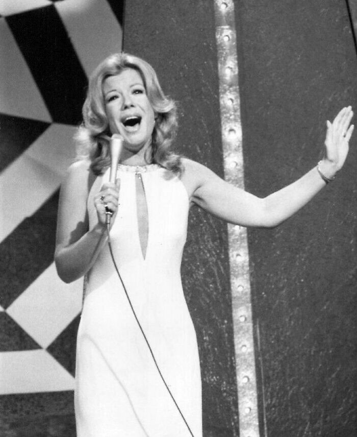 Vikki Carr on stage during a career highlight, singing into a microphone with her arm outstretched in a white dress.