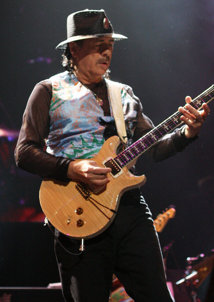 Carlos Santana playing electric guitar live, showcasing his iconic career highlights and musical passion.