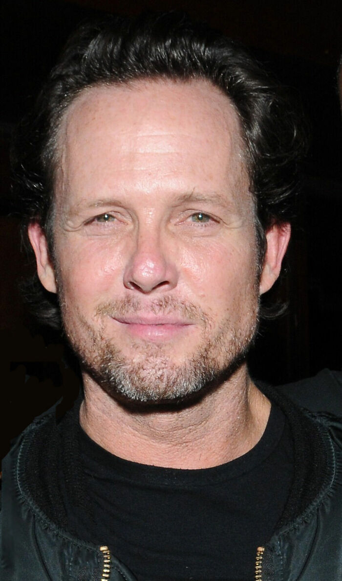 Dean Winters bio shows the actor looking at the camera, wearing a dark shirt. His career highlights include many famous roles.