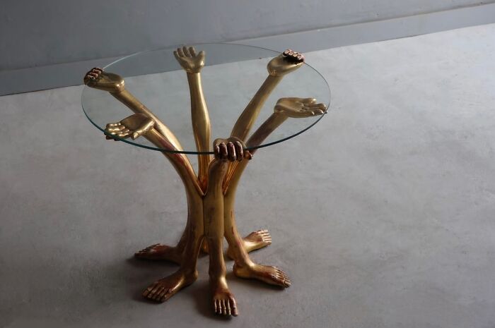 A gold, multi-limbed, bizarre furniture designer glass table on a grey floor.