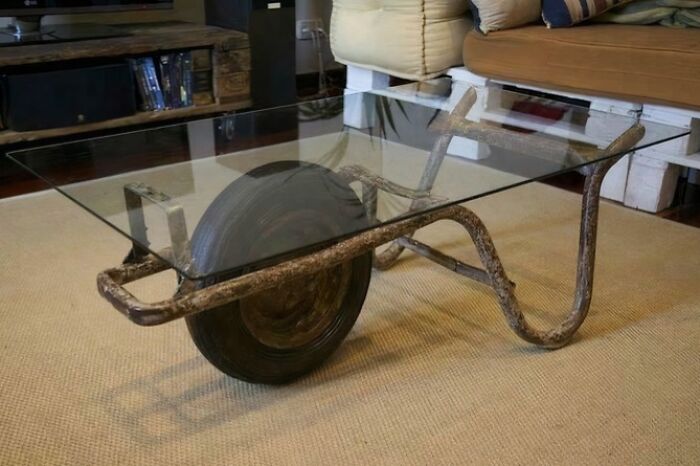 A wheelbarrow creatively repurposed into a glass-top coffee table, an example of bizarre furniture.