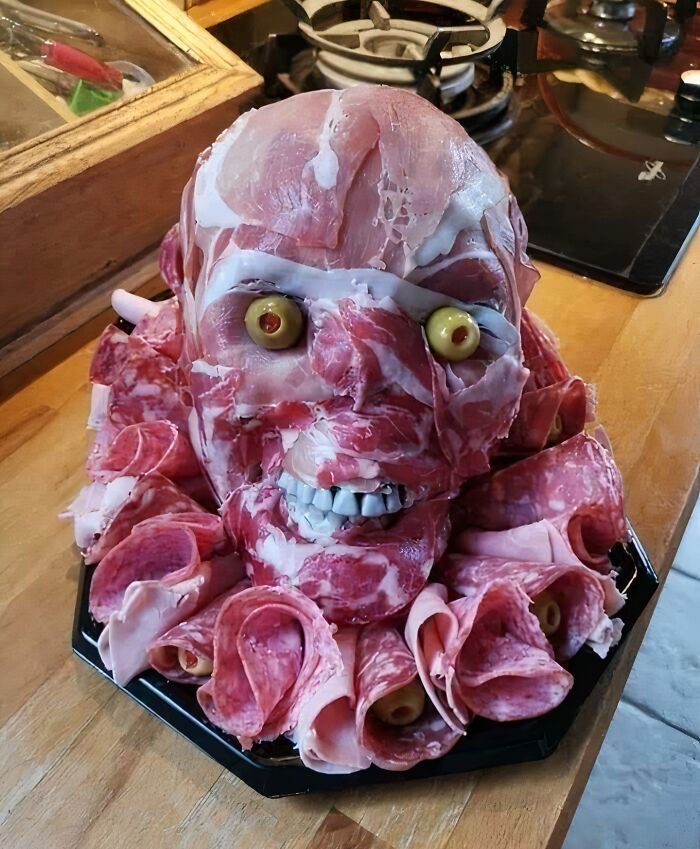 A head-shaped meat platter with olives for eyes and teeth, a creative yet potentially disgusting food presentation.
