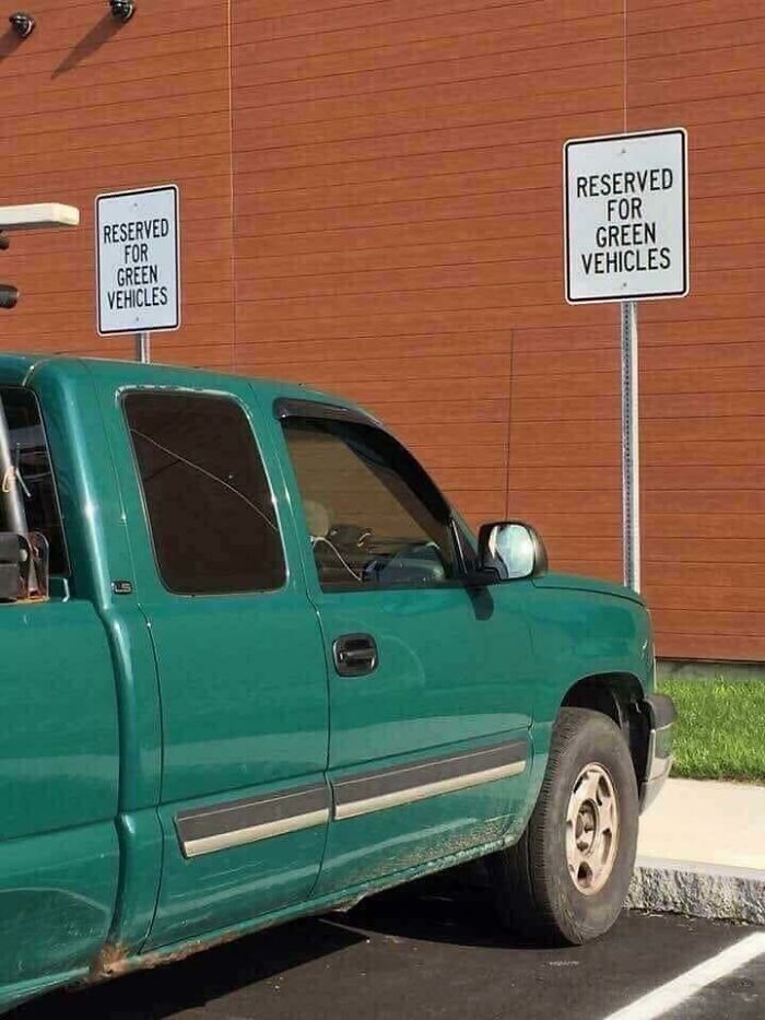 Outrageous parking of a green truck parked under a 'Reserved for Green Vehicles' sign, ironically.