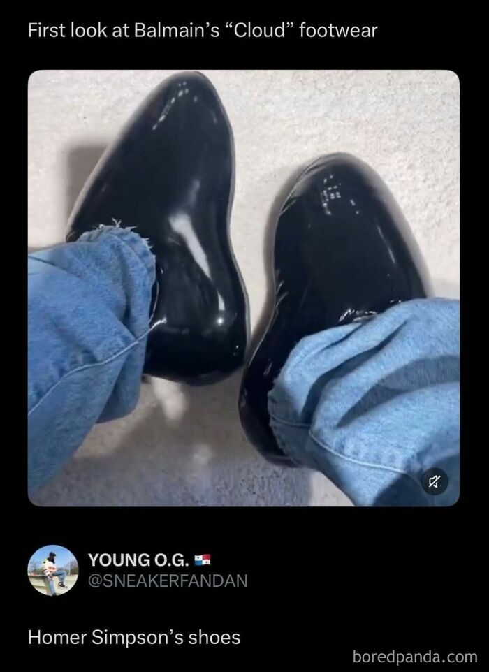 A pair of black, shiny Balmain Cloud footwear, resembling Homer Simpson's shoes, on someone's feet with blue jeans, a funny internet post.