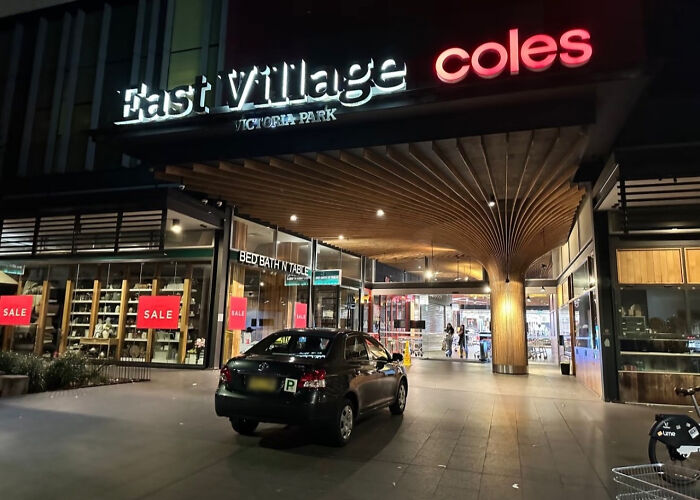 A black car parked directly in front of a Coles supermarket entrance, showcasing outrageous parking.