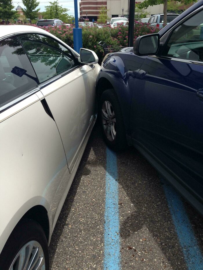 A white car and a blue SUV parked so close they are touching, an example of outrageous parking.