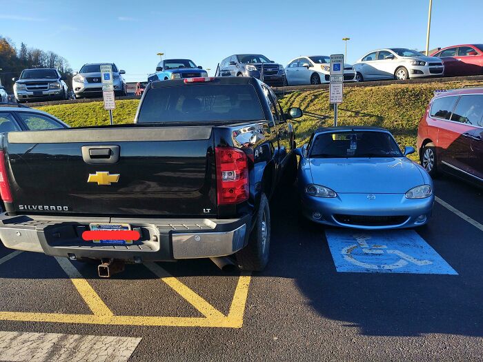 A black truck occupying two parking spaces next to a blue car in a disabled spot, showing outrageous parking.