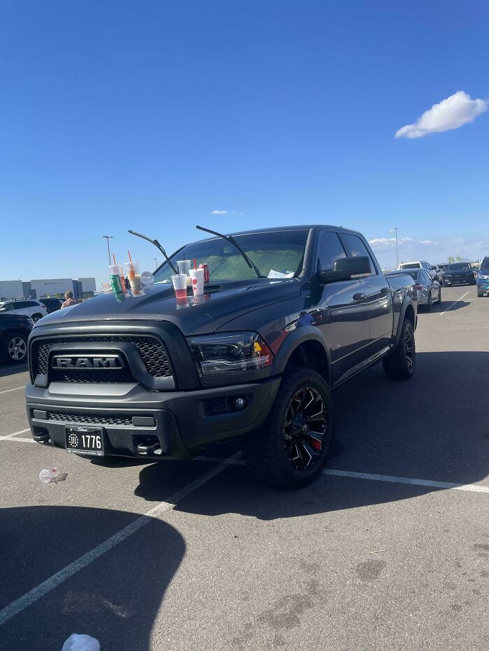 A black pickup truck parked with several drink cups on its windshield, displaying outrageous parking.