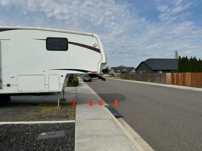 A large RV extends over the sidewalk with cones, showcasing outrageous parking.