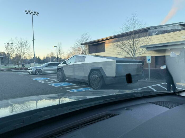 A Tesla Cybertruck is parked diagonally across multiple handicapped parking spots, an instance of outrageous parking.