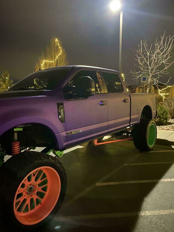 A purple, lifted Ford F-250 truck with large, colorful wheels is parked at night, displaying outrageous parking.