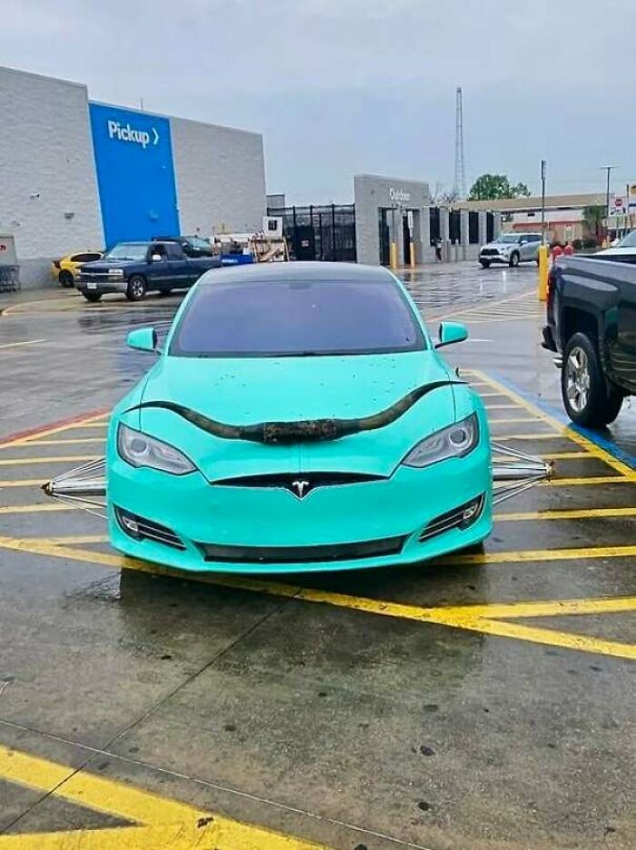 A teal Tesla with unusual spikes parked brazenly across multiple spaces, showcasing outrageous parking.