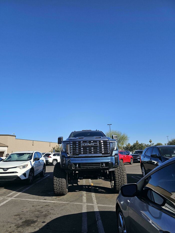 A massive lifted GMC truck takes up two parking spots, an example of outrageous parking.