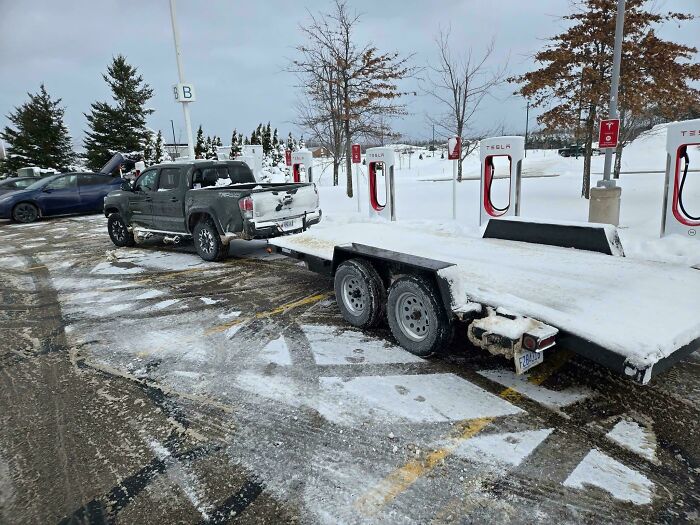 A pickup truck with a trailer taking up multiple Tesla charging spots, showing outrageous parking.
