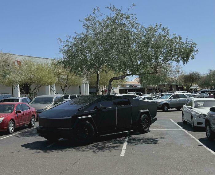 A black Cybertruck occupying two parking spaces in a lot, highlighting outrageous parking.