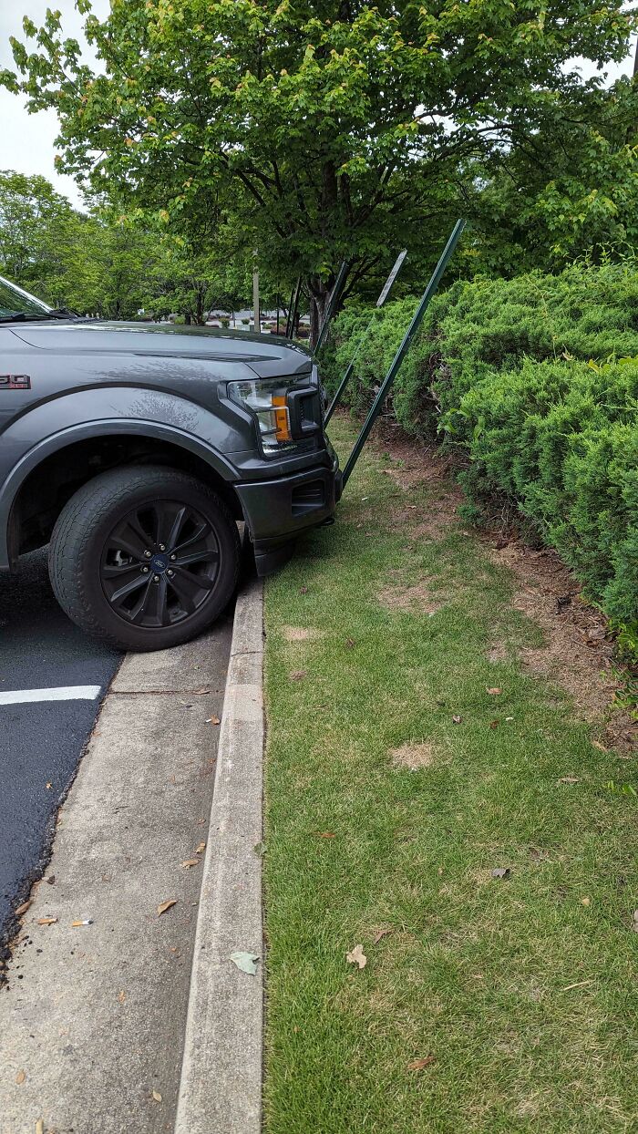 A grey SUV bumper close to a curb and bending two green poles, an example of outrageous parking.