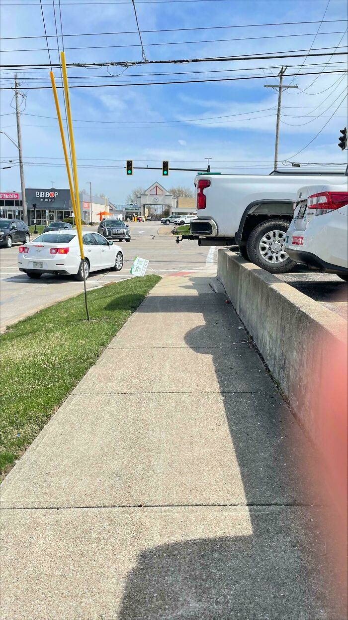 An outrageous parking job with a white pickup truck backed over a curb, blocking a sidewalk.