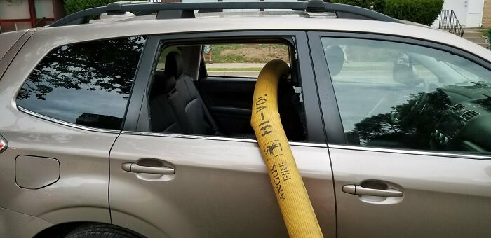 A beige SUV with a fire hose running through its partially open back window, highlighting outrageous parking.
