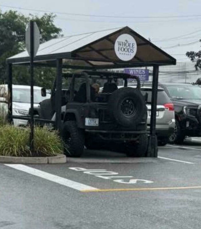 A black Jeep is parked under a Whole Foods sign, showcasing outrageous parking in a parking lot.