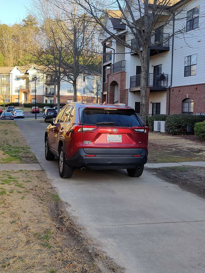 A red SUV parked partially on a sidewalk next to an apartment building, demonstrating outrageous parking.