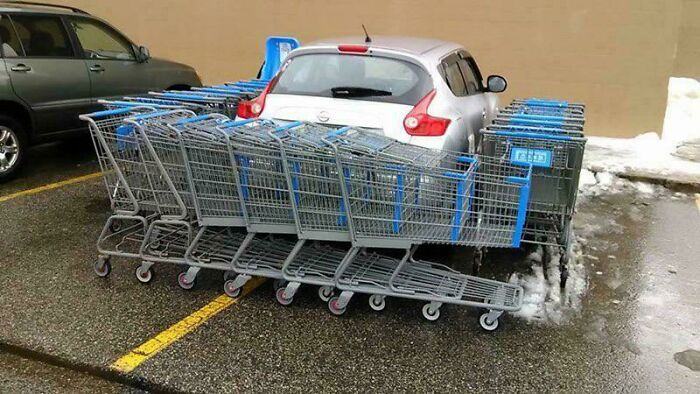 A silver car surrounded by shopping carts in a parking lot, showcasing outrageous parking.