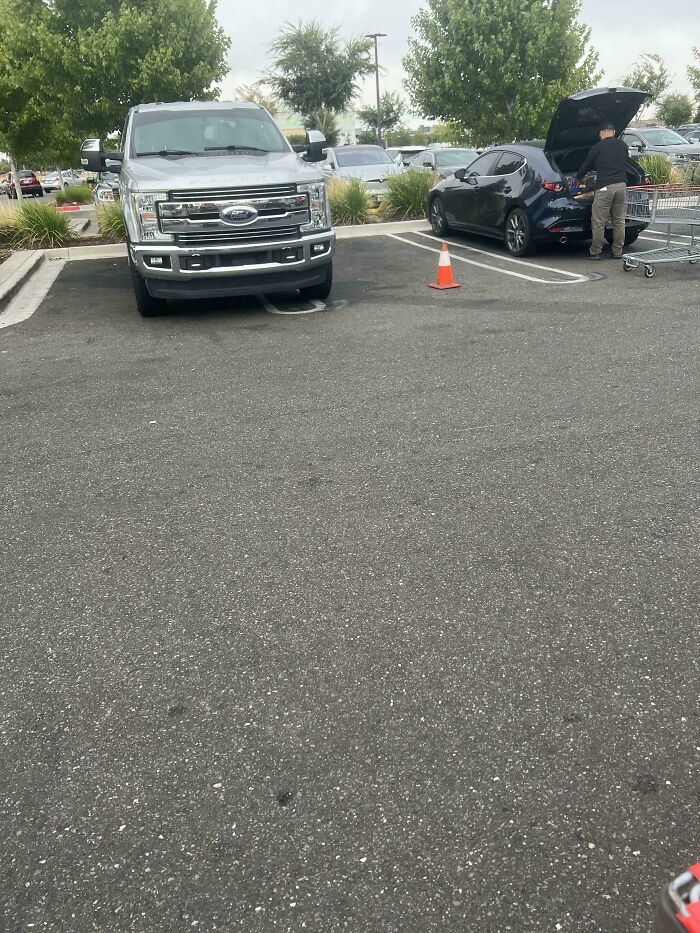 A silver pickup truck parked improperly, taking up multiple spots, showing outrageous parking.