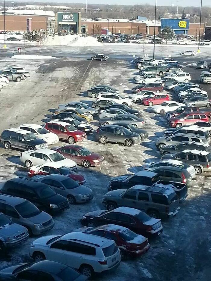 An aerial view of a snow-covered parking lot with cars parked haphazardly, highlighting outrageous parking arrangements.