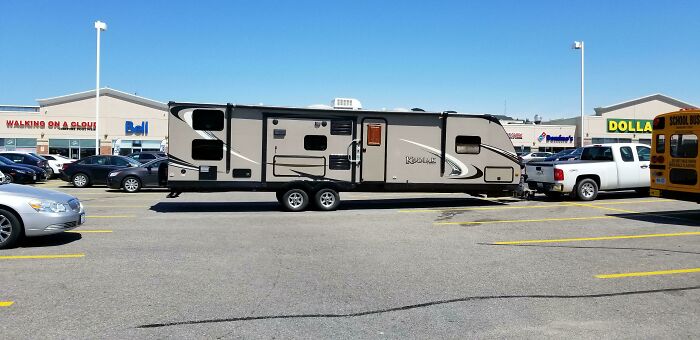 A recreational vehicle and truck taking up multiple spaces in a parking lot, an instance of outrageous parking.