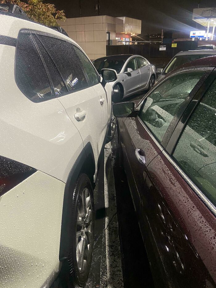 Two cars parked extremely close to each other in a parking lot, with barely any space between them, an example of outrageous parking.